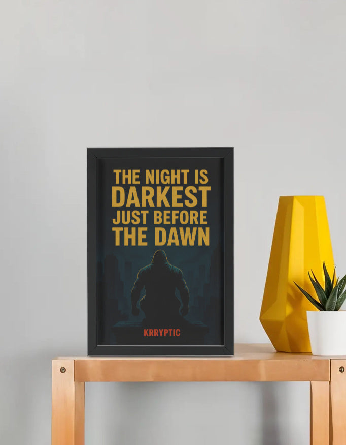Framed poster with text 'The night is darkest just before the dawn' on a table with a yellow vase and plant.